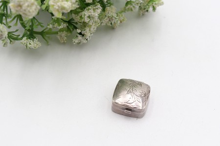 Caixa de comprimidos em prata com elementos vegetalistas gravados na tampa